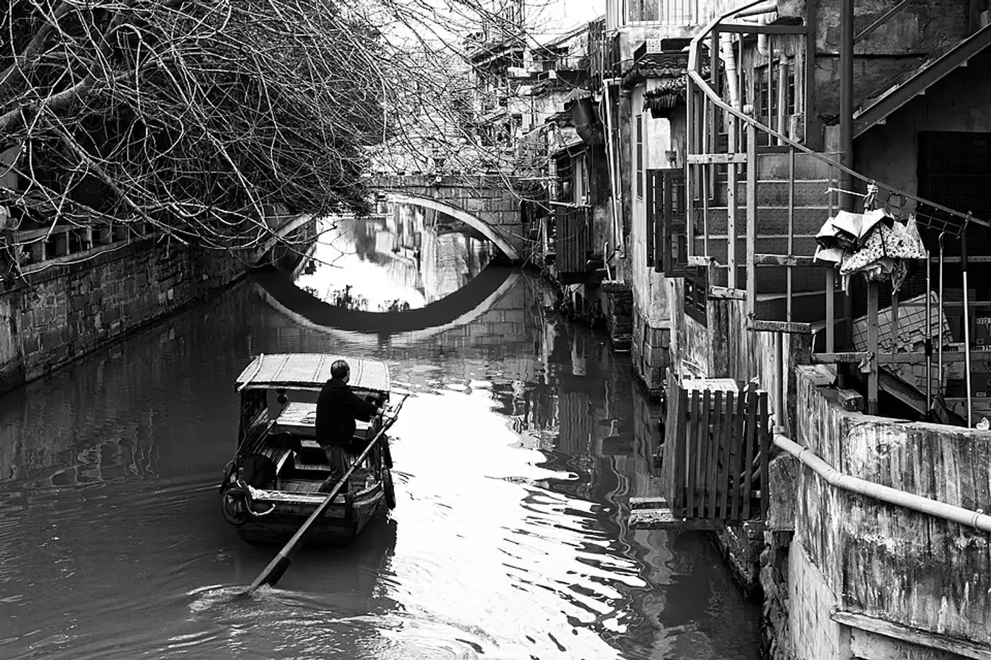 Barco navegando por um canal estreito entre casas antigas no centro de Suzhou